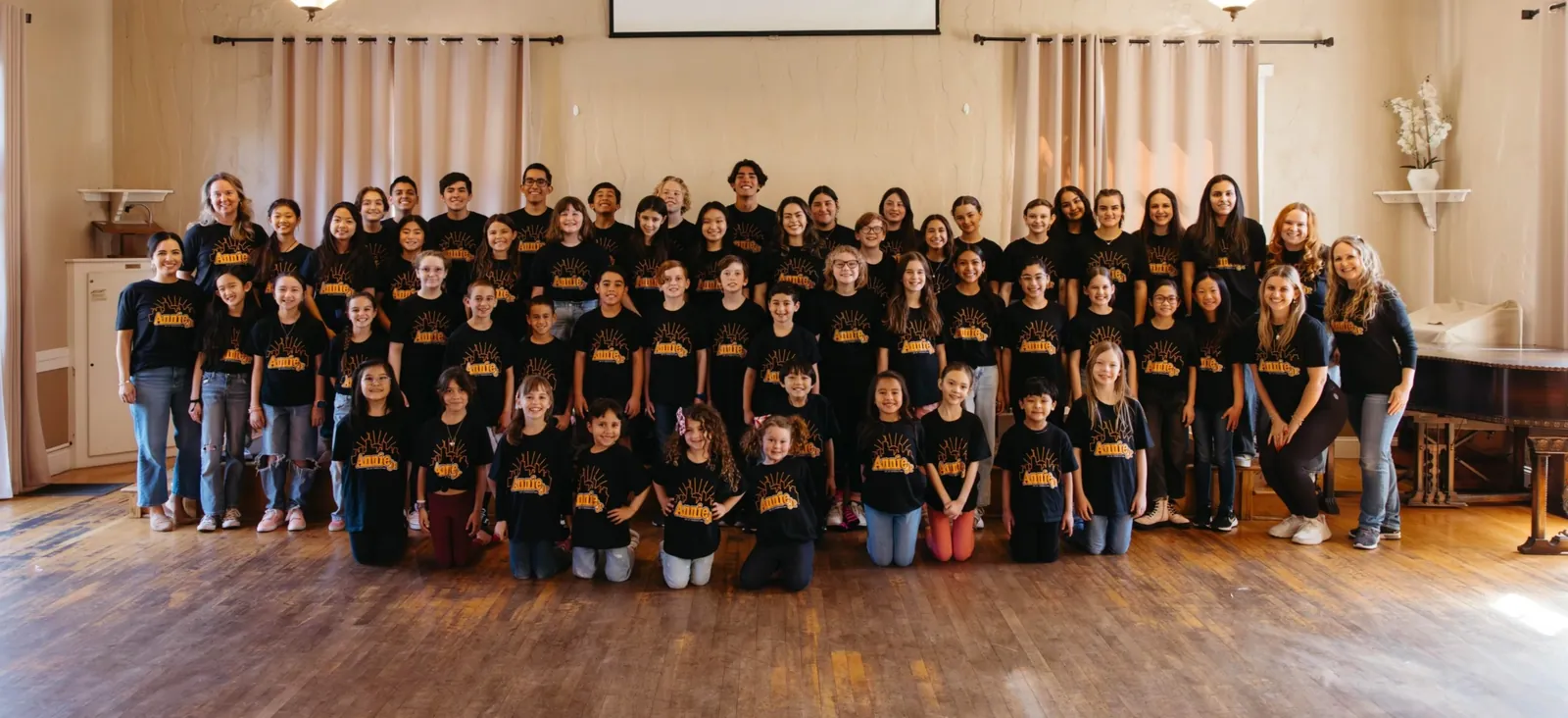 The A1 Musical Theatre cast in matching black T-shirts in a church hall